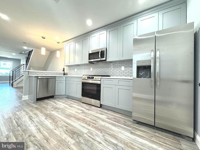 kitchen featuring kitchen peninsula, tasteful backsplash, stainless steel appliances, light hardwood / wood-style floors, and hanging light fixtures