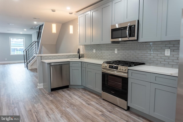 kitchen featuring kitchen peninsula, decorative light fixtures, stainless steel appliances, and gray cabinetry