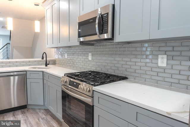 kitchen with backsplash, sink, hanging light fixtures, appliances with stainless steel finishes, and light stone counters