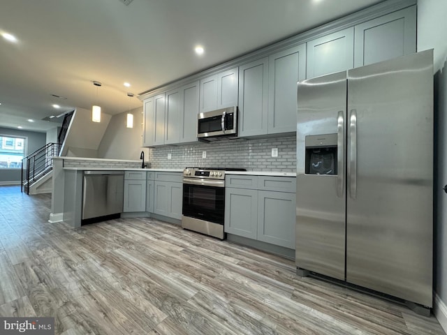 kitchen featuring gray cabinetry, tasteful backsplash, pendant lighting, appliances with stainless steel finishes, and light wood-type flooring