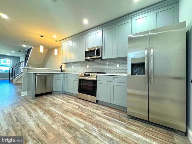 kitchen featuring backsplash, appliances with stainless steel finishes, decorative light fixtures, light hardwood / wood-style floors, and kitchen peninsula