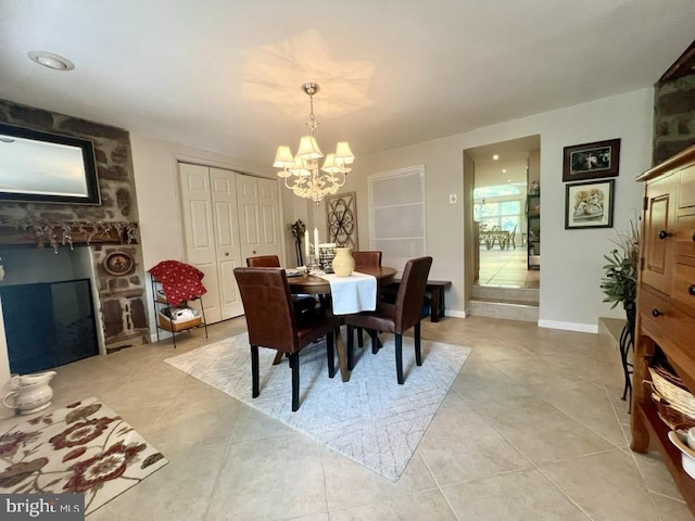 dining space featuring a stone fireplace, light tile patterned flooring, and a chandelier