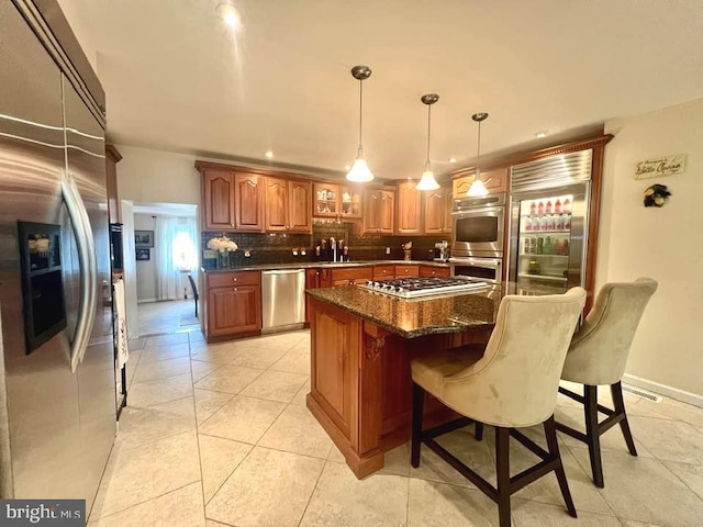 kitchen featuring light tile patterned floors, tasteful backsplash, a kitchen island, decorative light fixtures, and stainless steel appliances