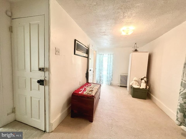 sitting room featuring radiator heating unit, a textured ceiling, and light carpet