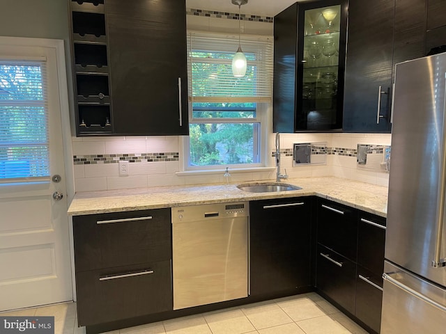 kitchen with pendant lighting, tasteful backsplash, sink, appliances with stainless steel finishes, and light stone countertops