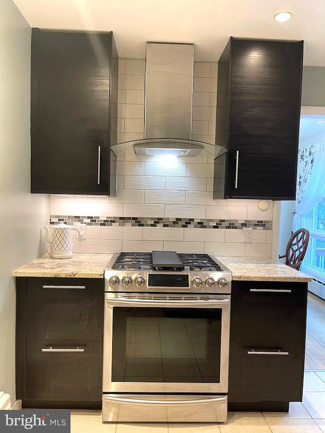 kitchen featuring light tile patterned flooring, light stone counters, tasteful backsplash, wall chimney exhaust hood, and stainless steel gas range oven