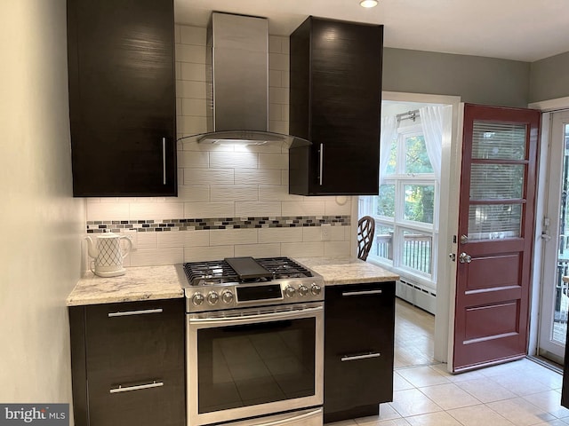 kitchen with light stone counters, backsplash, wall chimney range hood, stainless steel gas stove, and a baseboard heating unit