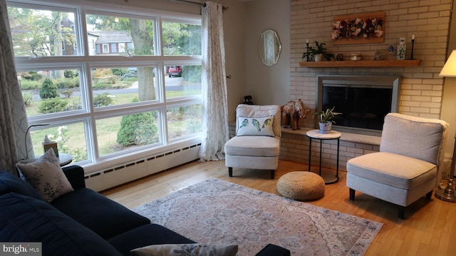 living room featuring a baseboard heating unit, light wood-type flooring, a healthy amount of sunlight, and a fireplace