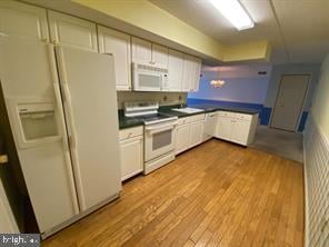 kitchen with white appliances, light hardwood / wood-style floors, and white cabinetry