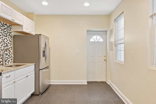 kitchen featuring white cabinets, backsplash, light stone countertops, stainless steel refrigerator with ice dispenser, and sink