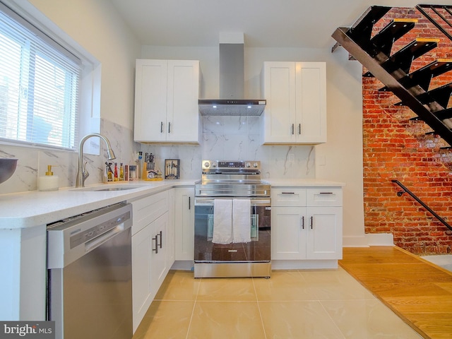 kitchen with stainless steel appliances, white cabinetry, wall chimney exhaust hood, and sink