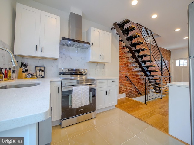 kitchen featuring stainless steel range with electric stovetop, white cabinets, sink, wall chimney exhaust hood, and light tile patterned floors