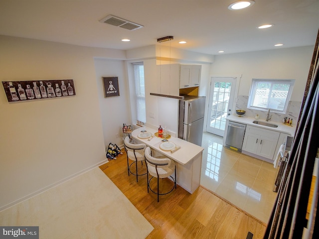 kitchen featuring white cabinetry, sink, stainless steel appliances, a kitchen breakfast bar, and light wood-type flooring