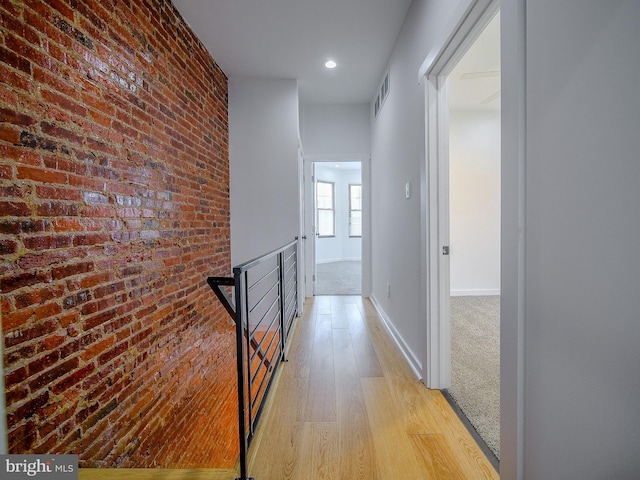 hall featuring light hardwood / wood-style flooring and brick wall