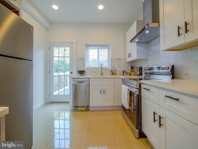 kitchen with white cabinets, wall chimney range hood, sink, decorative backsplash, and stainless steel appliances