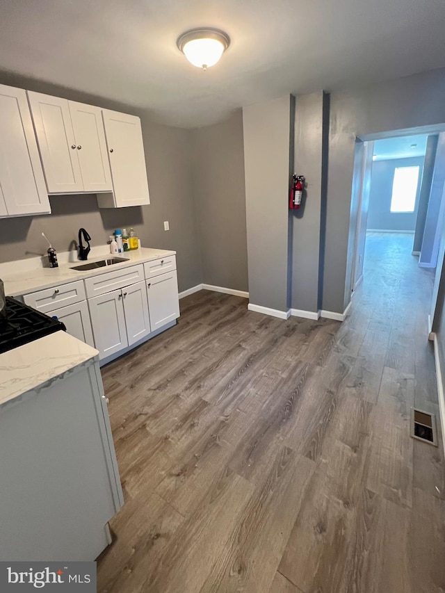 kitchen with light stone countertops, white cabinets, wood-type flooring, and stove