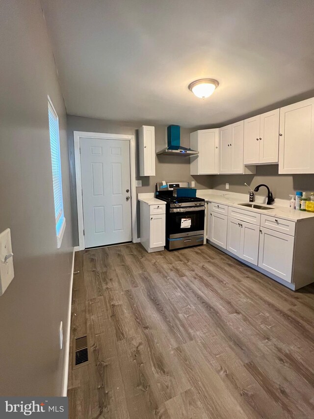 kitchen featuring sink, wall chimney exhaust hood, white cabinetry, stainless steel stove, and light wood-type flooring