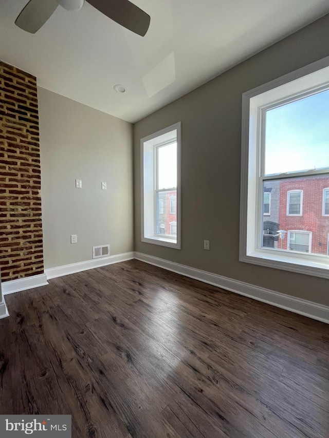 empty room featuring dark wood-type flooring, a healthy amount of sunlight, and brick wall