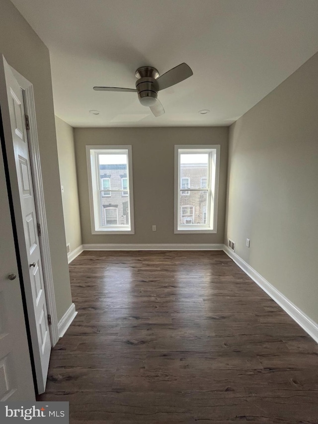 empty room featuring plenty of natural light, dark wood-type flooring, and ceiling fan