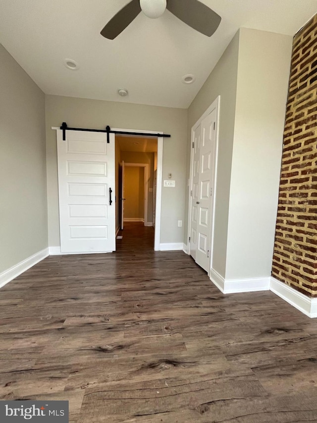 empty room featuring dark hardwood / wood-style floors, a barn door, brick wall, and ceiling fan