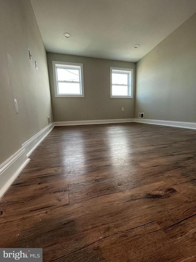 spare room featuring a healthy amount of sunlight and dark hardwood / wood-style flooring