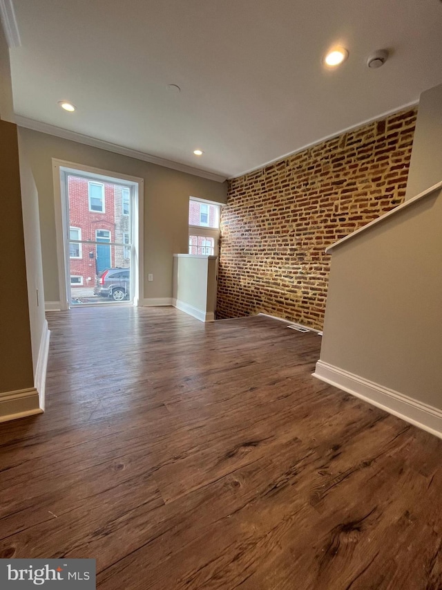 empty room with dark hardwood / wood-style flooring, crown molding, and brick wall