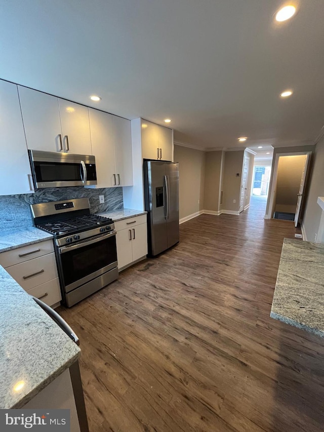 kitchen with light stone countertops, dark wood-type flooring, backsplash, appliances with stainless steel finishes, and ornamental molding