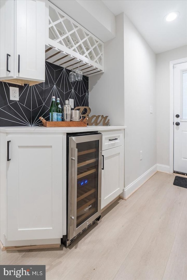 bar featuring white cabinets, wine cooler, light wood-type flooring, and backsplash