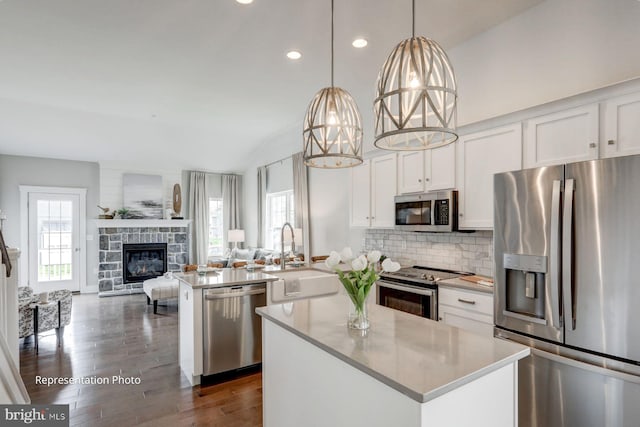 kitchen with stainless steel appliances, a center island with sink, a wealth of natural light, and a stone fireplace