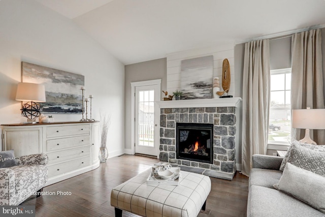 living room with vaulted ceiling, dark hardwood / wood-style floors, and a stone fireplace