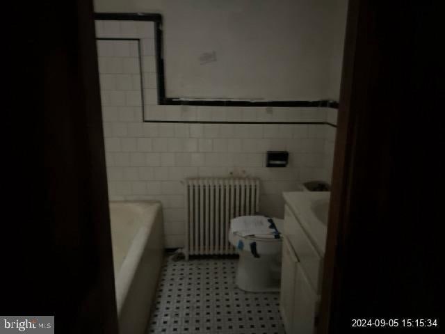 bathroom featuring tile walls, a washtub, radiator, vanity, and toilet