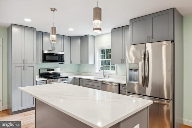 kitchen with sink, light hardwood / wood-style flooring, decorative light fixtures, light stone counters, and stainless steel appliances