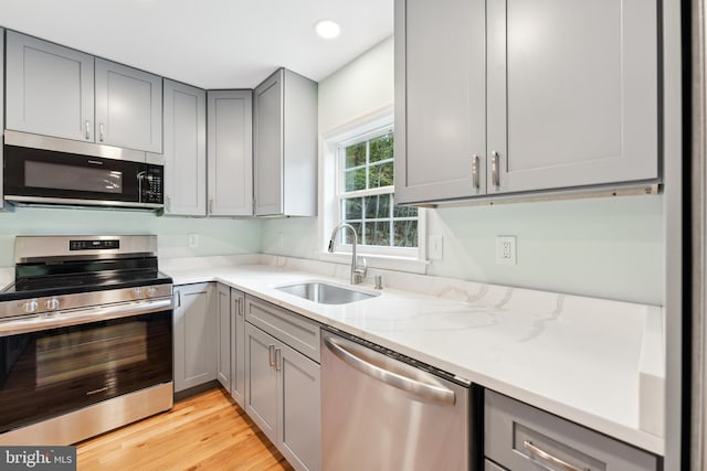 kitchen with light wood-type flooring, light stone counters, stainless steel appliances, sink, and gray cabinets