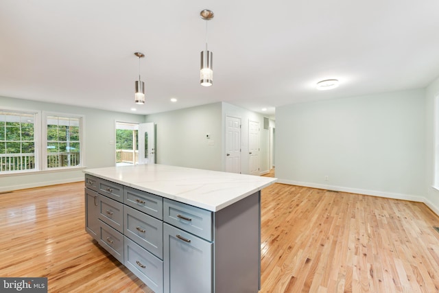 kitchen with pendant lighting, gray cabinetry, light hardwood / wood-style flooring, a kitchen island, and light stone counters