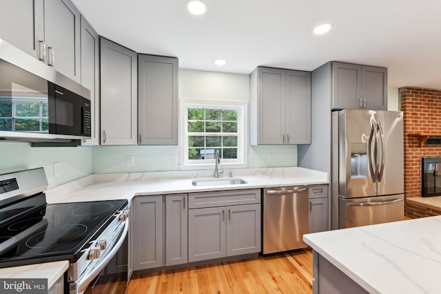 kitchen with light wood-type flooring, a brick fireplace, stainless steel appliances, sink, and gray cabinets