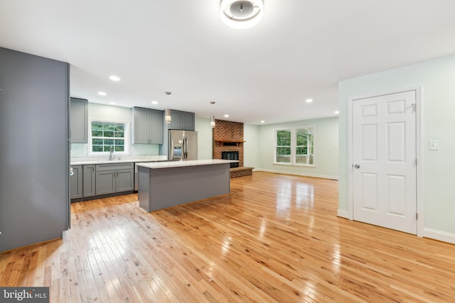 kitchen with hanging light fixtures, stainless steel fridge, an island with sink, gray cabinets, and light wood-type flooring