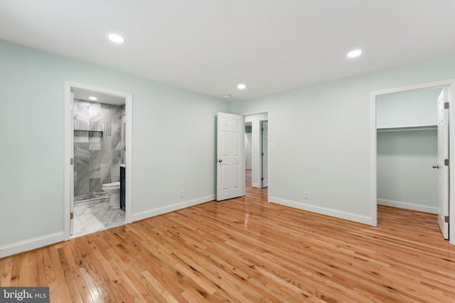 unfurnished bedroom featuring a closet, ensuite bath, a spacious closet, and light hardwood / wood-style flooring