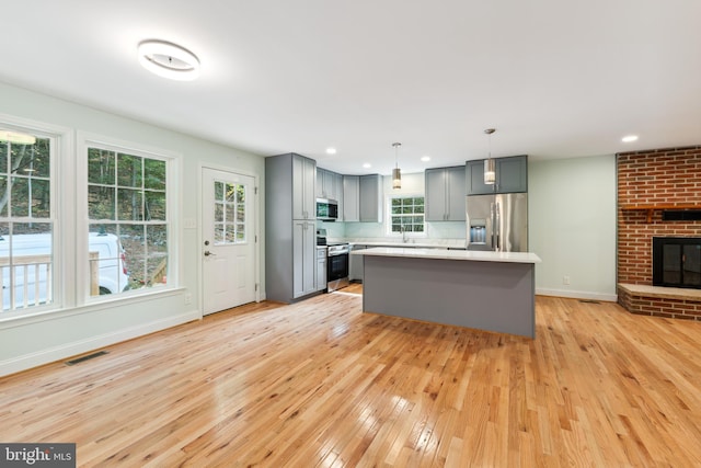 kitchen featuring gray cabinetry, stainless steel appliances, pendant lighting, a center island, and light hardwood / wood-style floors