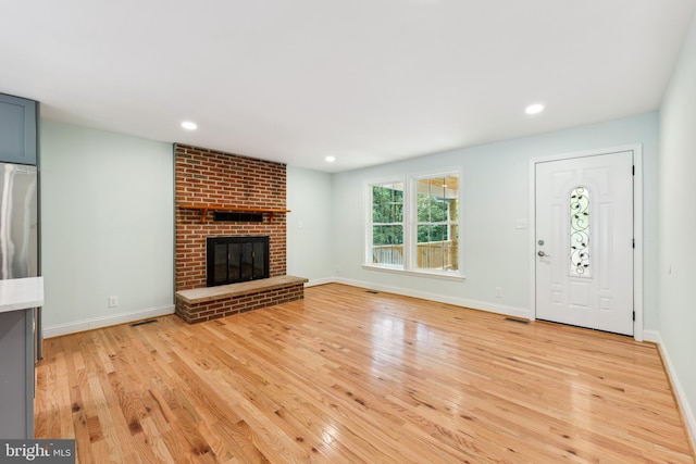 unfurnished living room featuring a brick fireplace and light hardwood / wood-style flooring