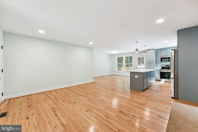 kitchen with appliances with stainless steel finishes, gray cabinetry, pendant lighting, light hardwood / wood-style flooring, and a kitchen island