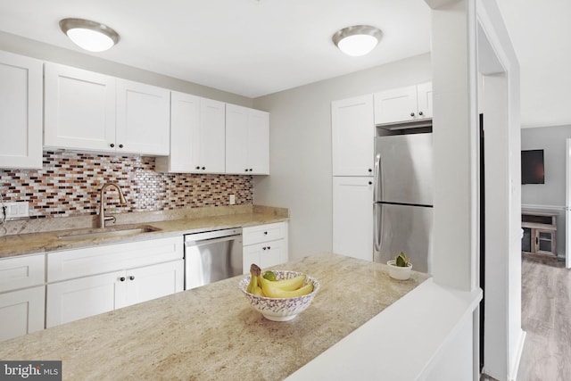 kitchen with light wood-type flooring, sink, white cabinetry, stainless steel appliances, and backsplash