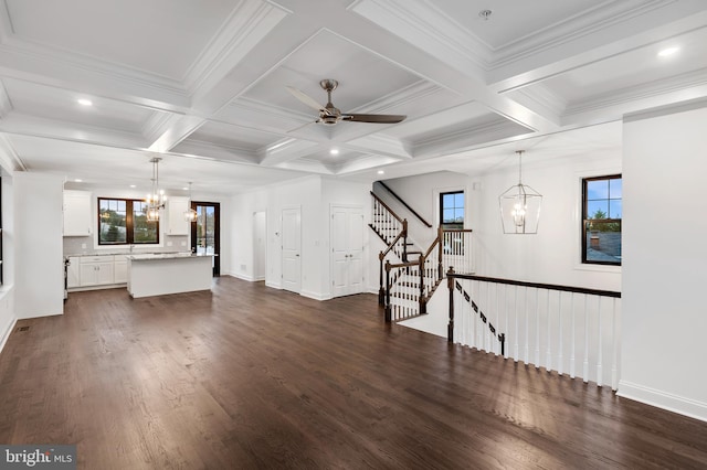 unfurnished living room featuring ceiling fan with notable chandelier, coffered ceiling, dark wood-type flooring, and a wealth of natural light