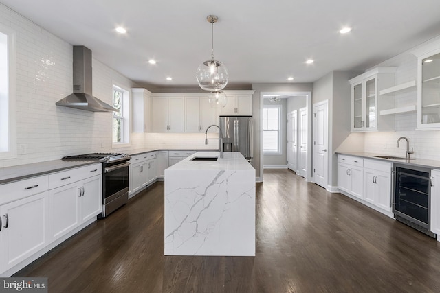 kitchen with a healthy amount of sunlight, appliances with stainless steel finishes, a kitchen island, and wall chimney range hood