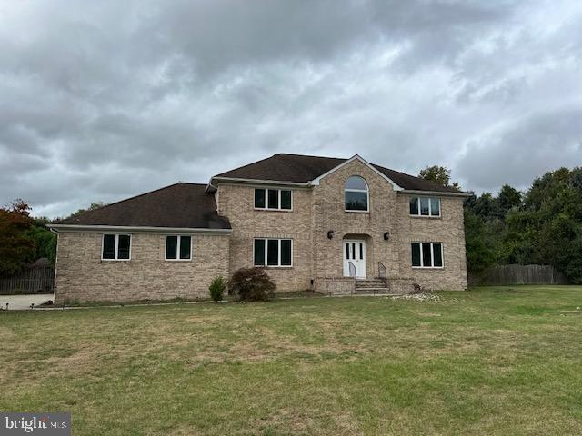 view of front of house featuring brick siding, fence, and a front lawn