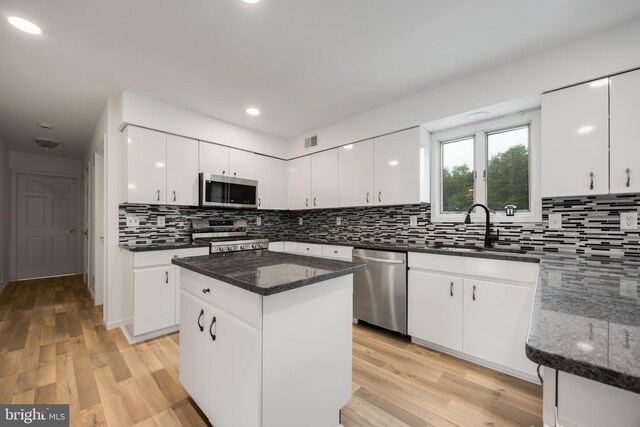 kitchen with stainless steel appliances, a center island, white cabinets, and dark stone countertops