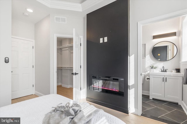 bedroom featuring sink, ornamental molding, a walk in closet, a closet, and dark hardwood / wood-style flooring