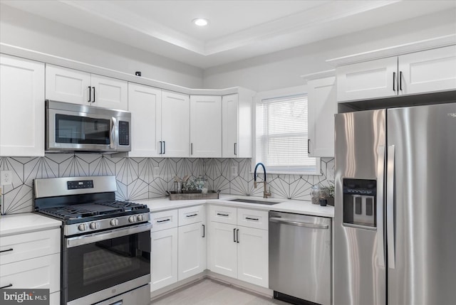 kitchen with white cabinets, sink, tasteful backsplash, stainless steel appliances, and a tray ceiling