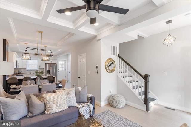 living room featuring ceiling fan with notable chandelier, crown molding, beam ceiling, and light hardwood / wood-style flooring