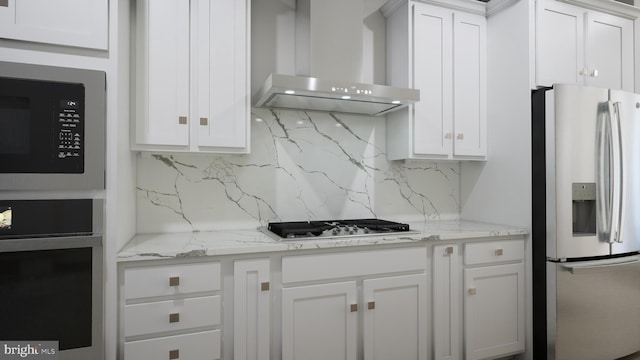 kitchen featuring white cabinetry, wall chimney range hood, backsplash, appliances with stainless steel finishes, and light stone countertops