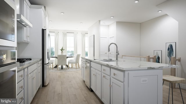 kitchen with white cabinetry, light stone counters, light wood-type flooring, a kitchen island with sink, and sink